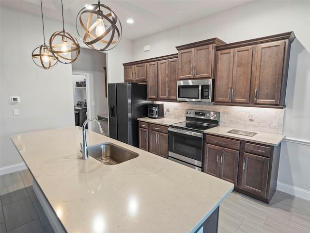 kitchen with a sink, dark brown cabinets, decorative backsplash, appliances with stainless steel finishes, and a kitchen island with sink