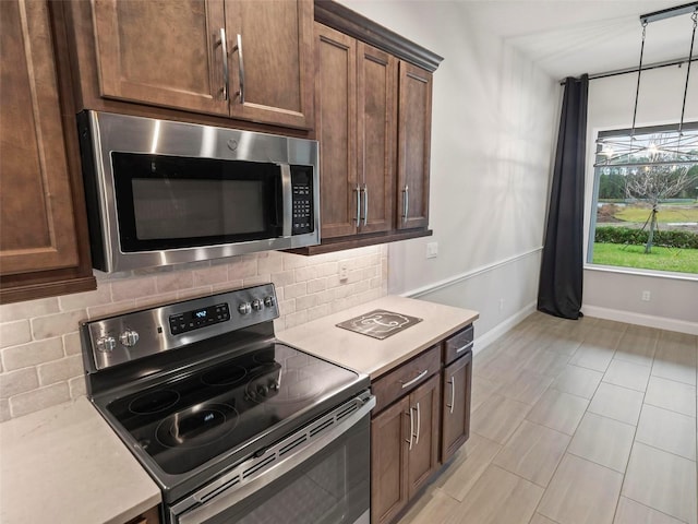 kitchen with baseboards, decorative light fixtures, light countertops, decorative backsplash, and appliances with stainless steel finishes