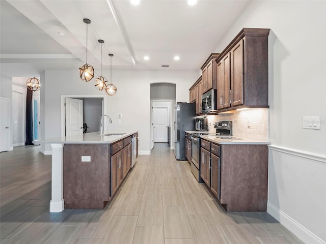 kitchen featuring a sink, light countertops, decorative backsplash, appliances with stainless steel finishes, and a kitchen island with sink