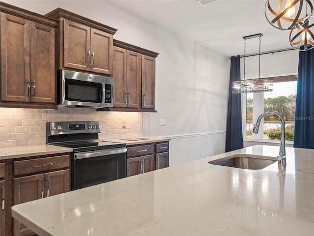 kitchen with light stone countertops, a sink, hanging light fixtures, appliances with stainless steel finishes, and backsplash