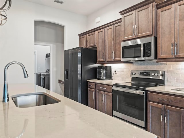 kitchen featuring washer and clothes dryer, appliances with stainless steel finishes, tasteful backsplash, and a sink