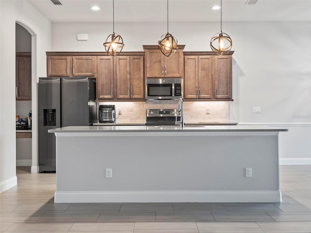 kitchen featuring stainless steel appliances, a kitchen island with sink, decorative backsplash, and hanging light fixtures