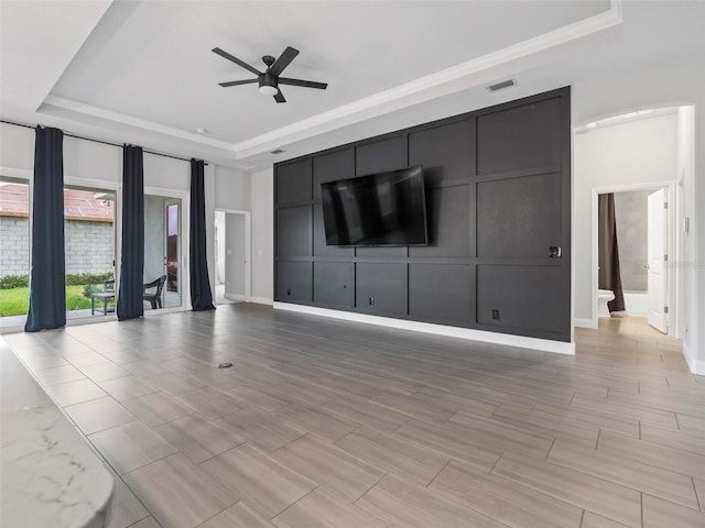 unfurnished living room with baseboards, a raised ceiling, a ceiling fan, and a decorative wall