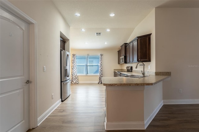 kitchen featuring lofted ceiling, stainless steel appliances, dark brown cabinetry, kitchen peninsula, and light wood-type flooring