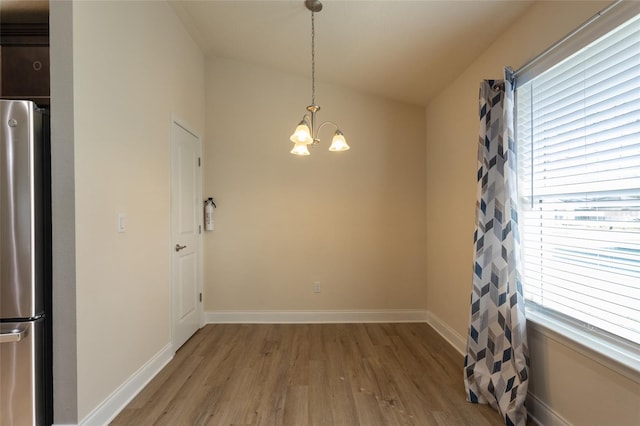 unfurnished dining area with lofted ceiling, a notable chandelier, and light wood-type flooring