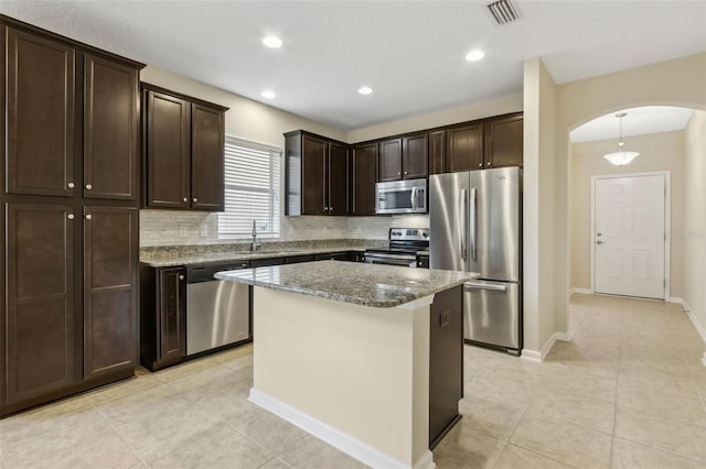 kitchen with stainless steel appliances, decorative backsplash, dark stone counters, pendant lighting, and a center island