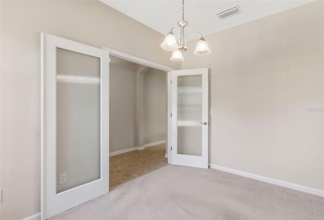 carpeted empty room featuring french doors and a notable chandelier