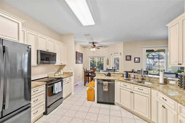 kitchen with light tile patterned flooring, appliances with stainless steel finishes, cream cabinets, sink, and light stone countertops