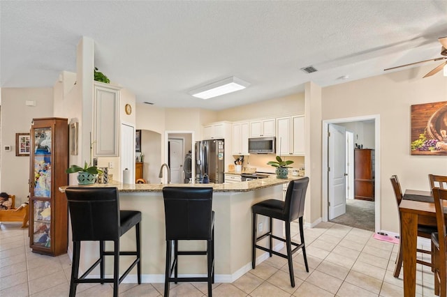 kitchen featuring stainless steel appliances, a breakfast bar, light tile patterned floors, and kitchen peninsula