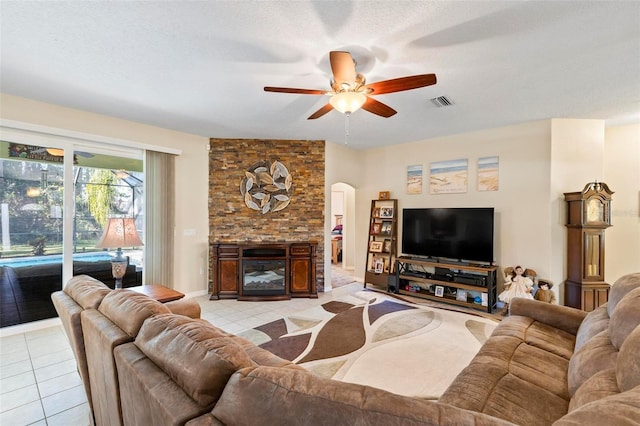 living room with ceiling fan, a large fireplace, a textured ceiling, and light tile patterned floors