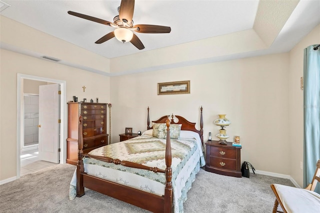 carpeted bedroom featuring ceiling fan, ensuite bath, and a tray ceiling