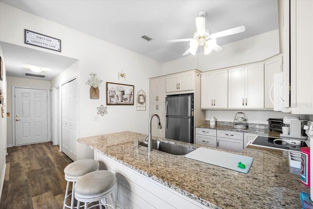 kitchen with white cabinets, a kitchen breakfast bar, kitchen peninsula, and stainless steel refrigerator