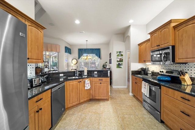 kitchen featuring appliances with stainless steel finishes, dark stone counters, sink, decorative light fixtures, and a notable chandelier