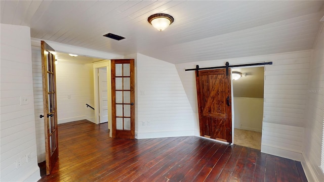 unfurnished room featuring a barn door, dark hardwood / wood-style flooring, lofted ceiling, and wooden walls