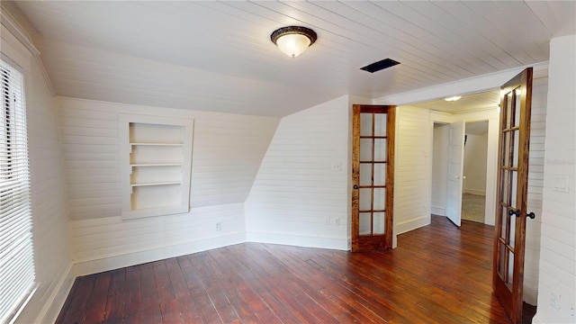 unfurnished room featuring french doors, built in features, dark hardwood / wood-style floors, wood walls, and vaulted ceiling