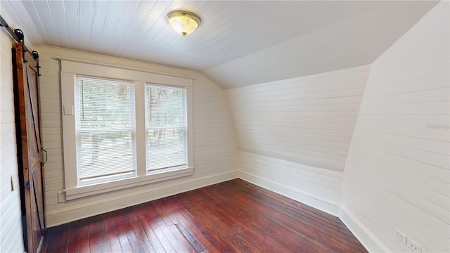 additional living space with dark hardwood / wood-style flooring, wooden walls, a barn door, and lofted ceiling