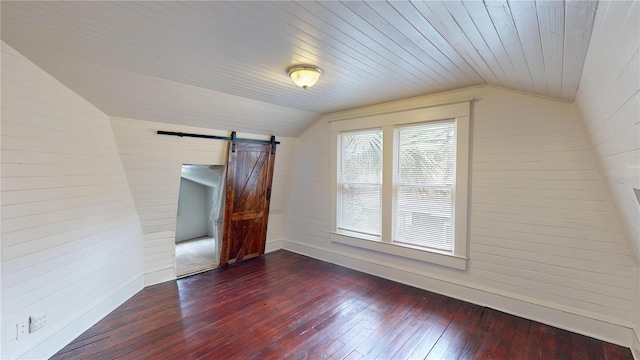 interior space featuring a barn door, dark wood-type flooring, wooden walls, and vaulted ceiling