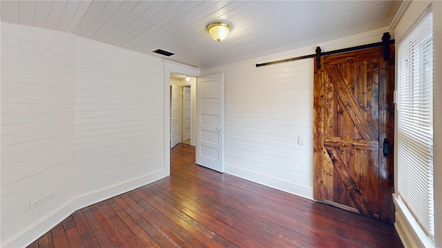 unfurnished bedroom with wood walls, a barn door, and dark hardwood / wood-style flooring