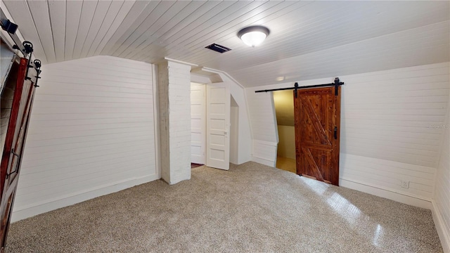 bonus room with a barn door, carpet floors, vaulted ceiling, and wood walls