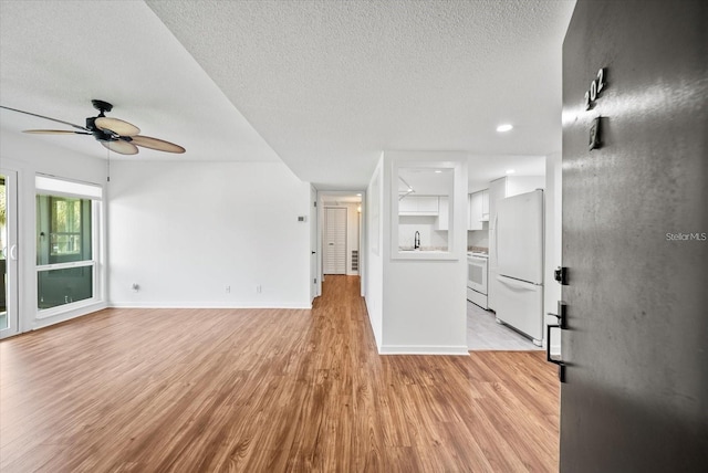 unfurnished living room with a textured ceiling, ceiling fan, light hardwood / wood-style floors, and sink