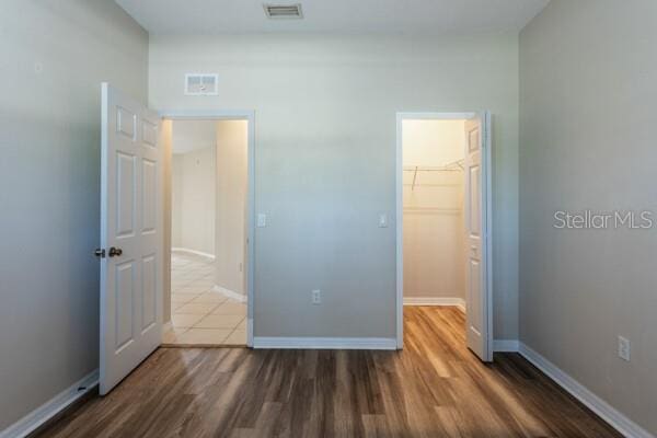 unfurnished bedroom with wood-type flooring, a spacious closet, and a closet