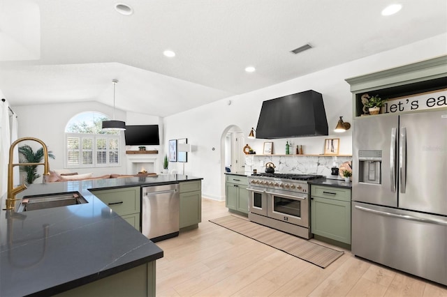 kitchen featuring sink, green cabinets, range hood, lofted ceiling, and appliances with stainless steel finishes