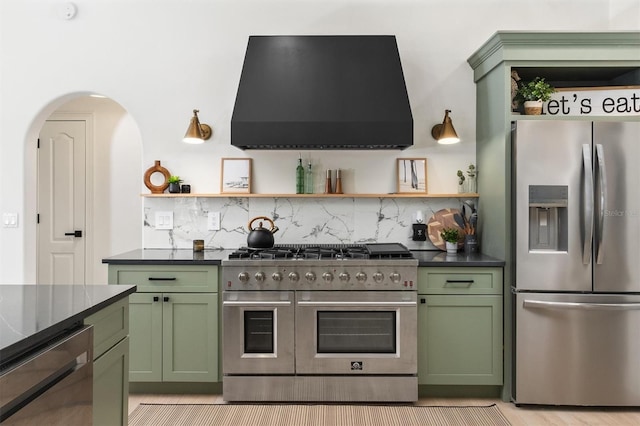 kitchen with green cabinets, decorative backsplash, extractor fan, and appliances with stainless steel finishes