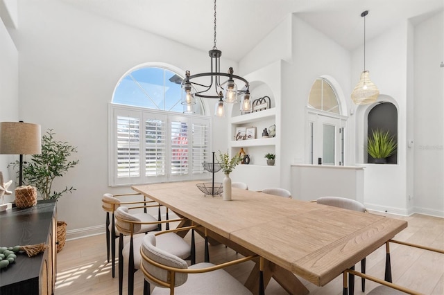 dining room featuring a chandelier, built in shelves, light hardwood / wood-style floors, and lofted ceiling