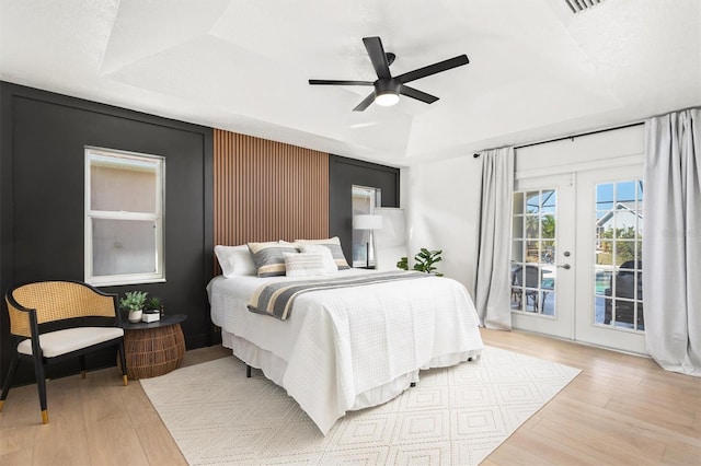 bedroom featuring access to exterior, ceiling fan, french doors, light hardwood / wood-style flooring, and a tray ceiling