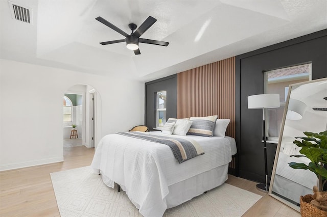 bedroom with a raised ceiling, ceiling fan, and light hardwood / wood-style floors