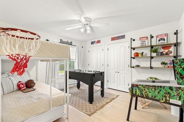 bedroom with a textured ceiling, light hardwood / wood-style flooring, ceiling fan, and multiple closets