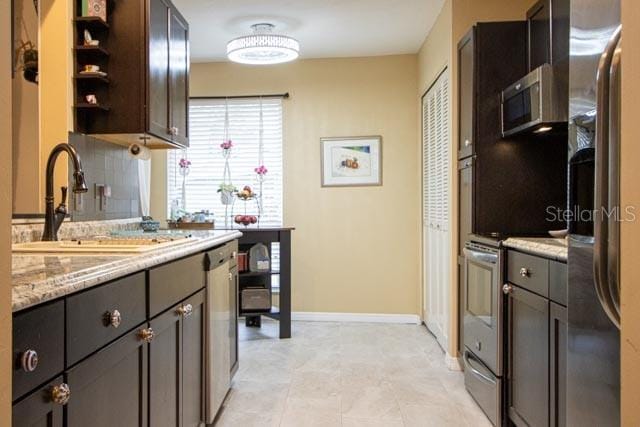 kitchen with stainless steel appliances, sink, backsplash, light stone counters, and dark brown cabinets