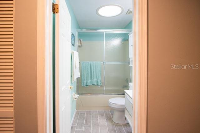 full bathroom featuring toilet, enclosed tub / shower combo, wood-type flooring, and vanity