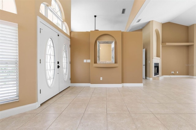 foyer entrance featuring a glass covered fireplace, light tile patterned flooring, and baseboards