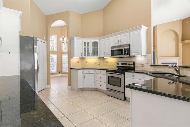 kitchen featuring glass insert cabinets, appliances with stainless steel finishes, a high ceiling, white cabinetry, and a sink