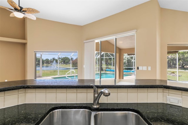 kitchen with a ceiling fan, vaulted ceiling, a sink, and dark stone countertops