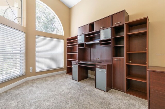 unfurnished office with baseboards, plenty of natural light, a towering ceiling, and light colored carpet