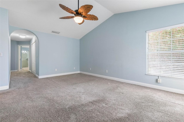 carpeted empty room featuring arched walkways, lofted ceiling, visible vents, a ceiling fan, and baseboards