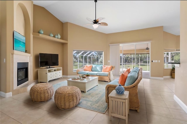 living room featuring light tile patterned floors, high vaulted ceiling, a ceiling fan, baseboards, and a glass covered fireplace