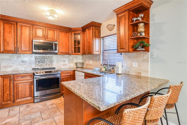 kitchen featuring sink, stainless steel appliances, light stone counters, kitchen peninsula, and a breakfast bar area