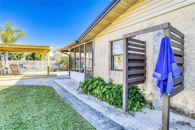 view of property exterior featuring a patio, a deck, a lawn, and a sunroom