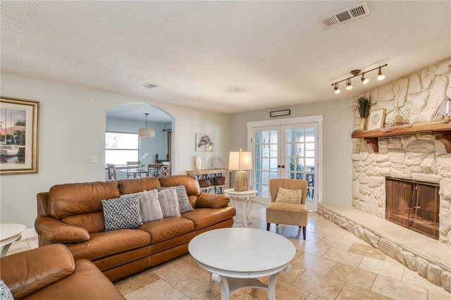 living room with french doors, a stone fireplace, plenty of natural light, and a textured ceiling