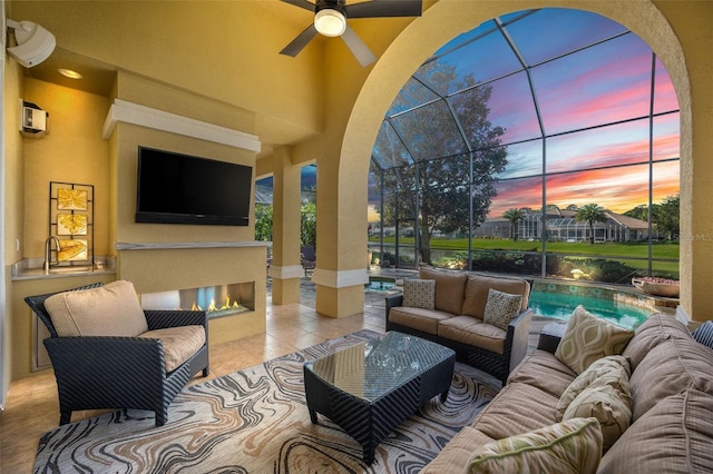 view of patio featuring ceiling fan, glass enclosure, and an outdoor living space with a fireplace