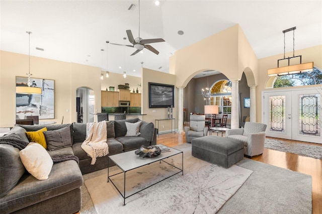 living room featuring light hardwood / wood-style floors, french doors, high vaulted ceiling, and ceiling fan with notable chandelier