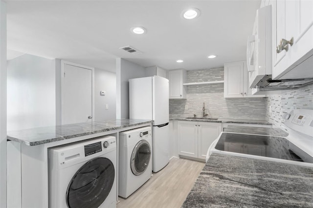 clothes washing area with sink, washing machine and dryer, and light hardwood / wood-style floors