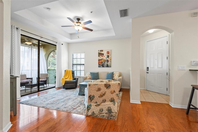 living room featuring a tray ceiling, light hardwood / wood-style flooring, and ceiling fan