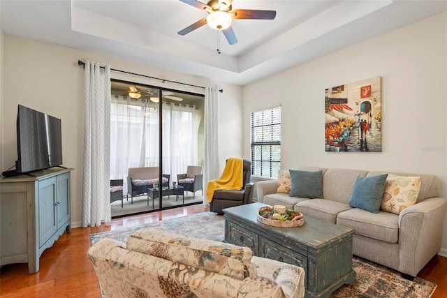 living room with ceiling fan, a raised ceiling, and wood-type flooring