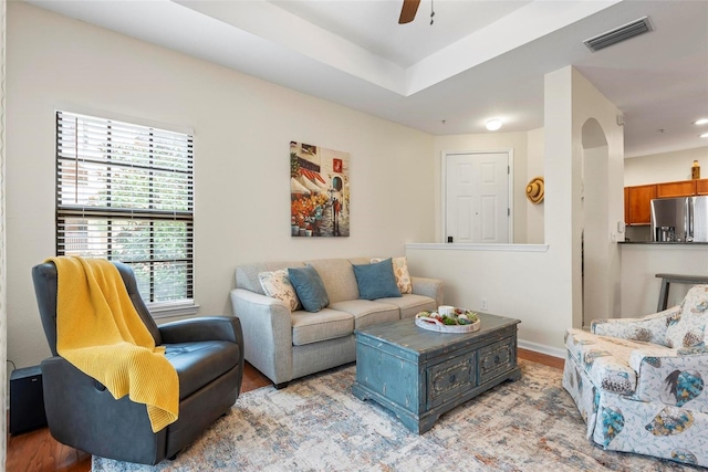 living room featuring light hardwood / wood-style floors, a raised ceiling, and ceiling fan