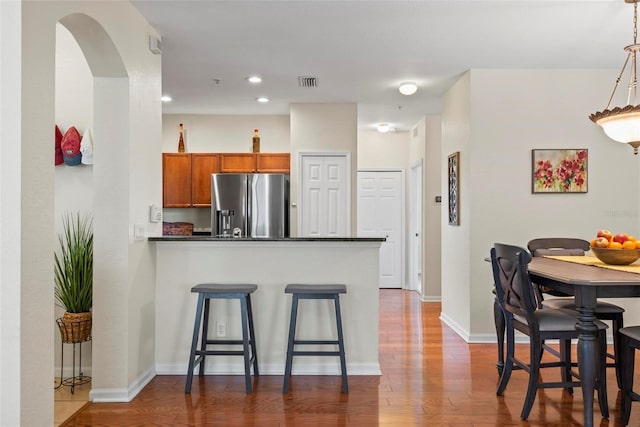 kitchen featuring a kitchen breakfast bar, kitchen peninsula, stainless steel fridge, hardwood / wood-style floors, and decorative light fixtures