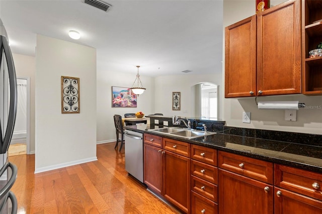 kitchen with stainless steel appliances, sink, decorative light fixtures, light hardwood / wood-style flooring, and dark stone countertops